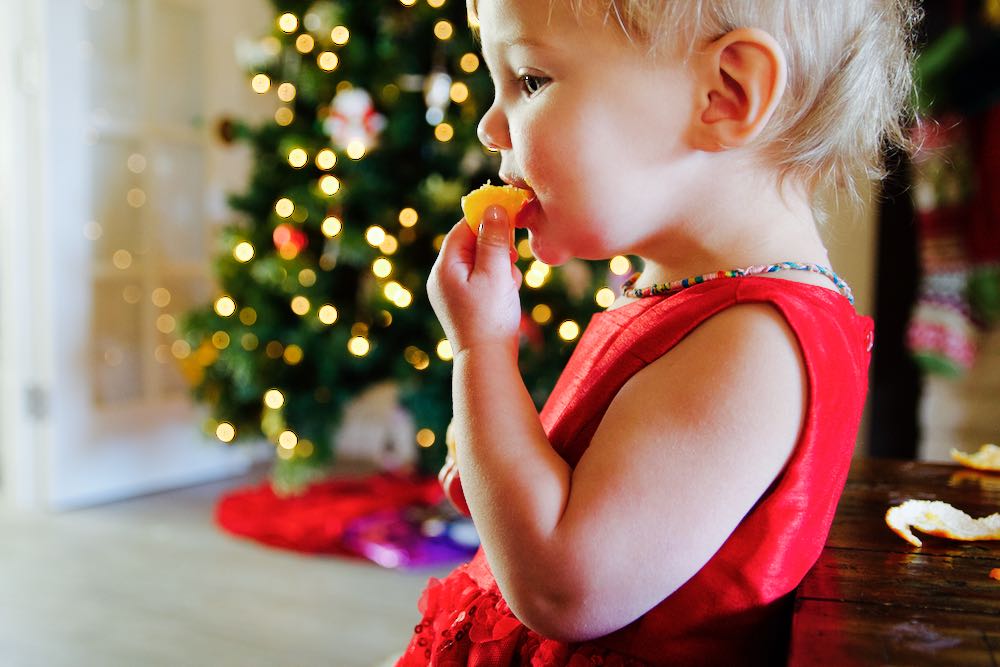 little girl eating orange in front of the christmas tree